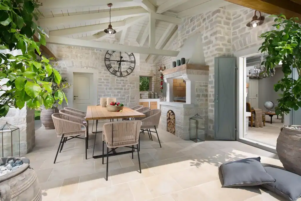 Überdachte Terrasse der Villa Elena mit Esstisch, Wanduhr und gemauertem Kamin