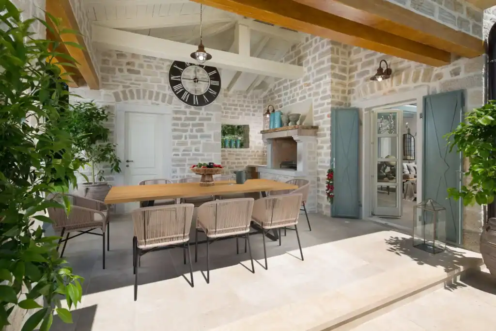 Überdachte Terrasse der Villa Nevia mit Esstisch, Rattanstühlen und Wanduhr