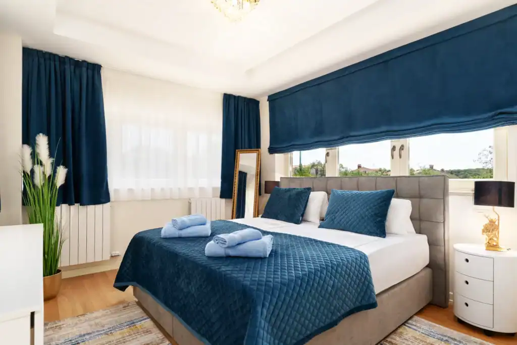 Schlafzimmer der Villa Lionea mit dunkelblauen Vorhängen und blauem Bettüberwurf