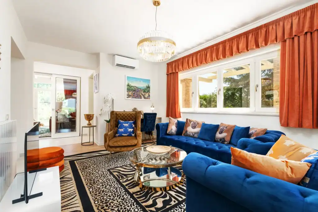 Wohnzimmer der Villa Lionea mit blauem Ecksofa und orangefarbenen Vorhängen